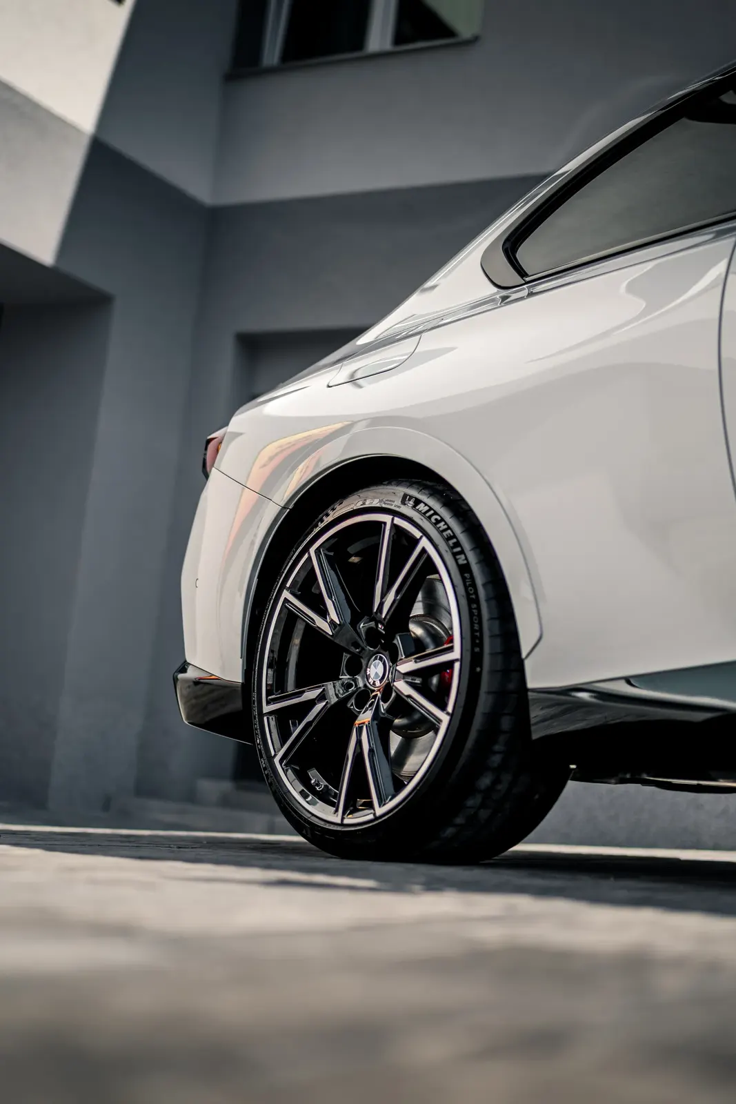 Detail of the rear wheel arch and wheel of a white BMW with a Michelin tyre against a grey facade.