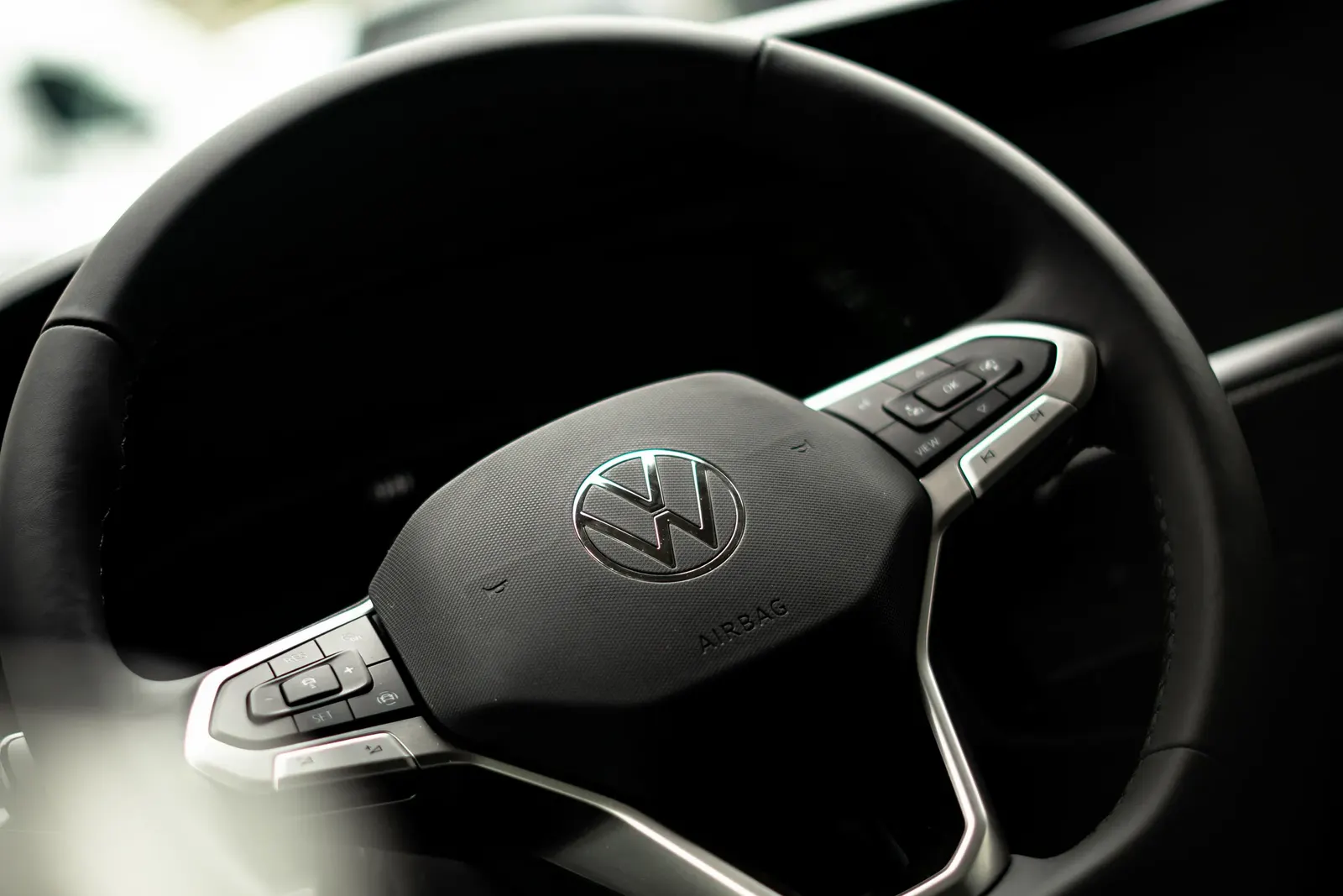Detail volantu Volkswagen se středovým logem VW a ovládacími tlačítky.