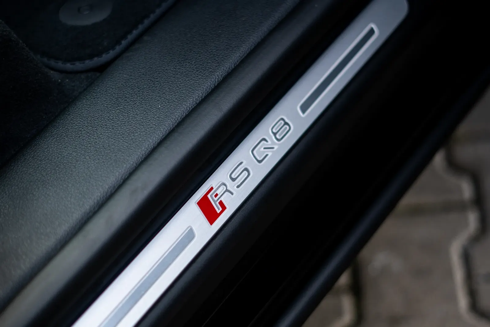 Close-up of a door-sill plate with the RS Q8 badge by the open car door.