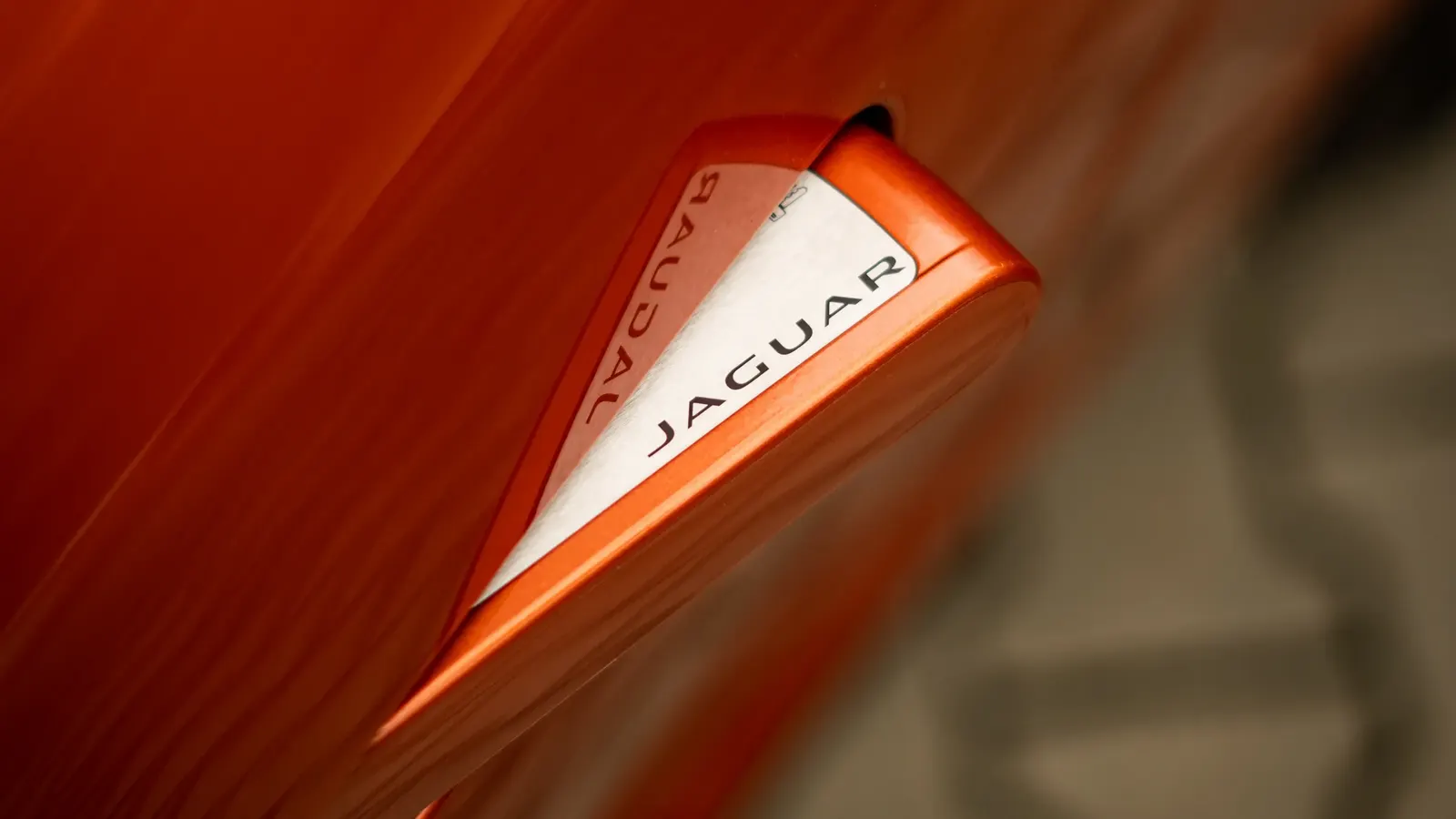 Detail vysunuté kliky dveří s nápisem Jaguar na oranžovém voze.