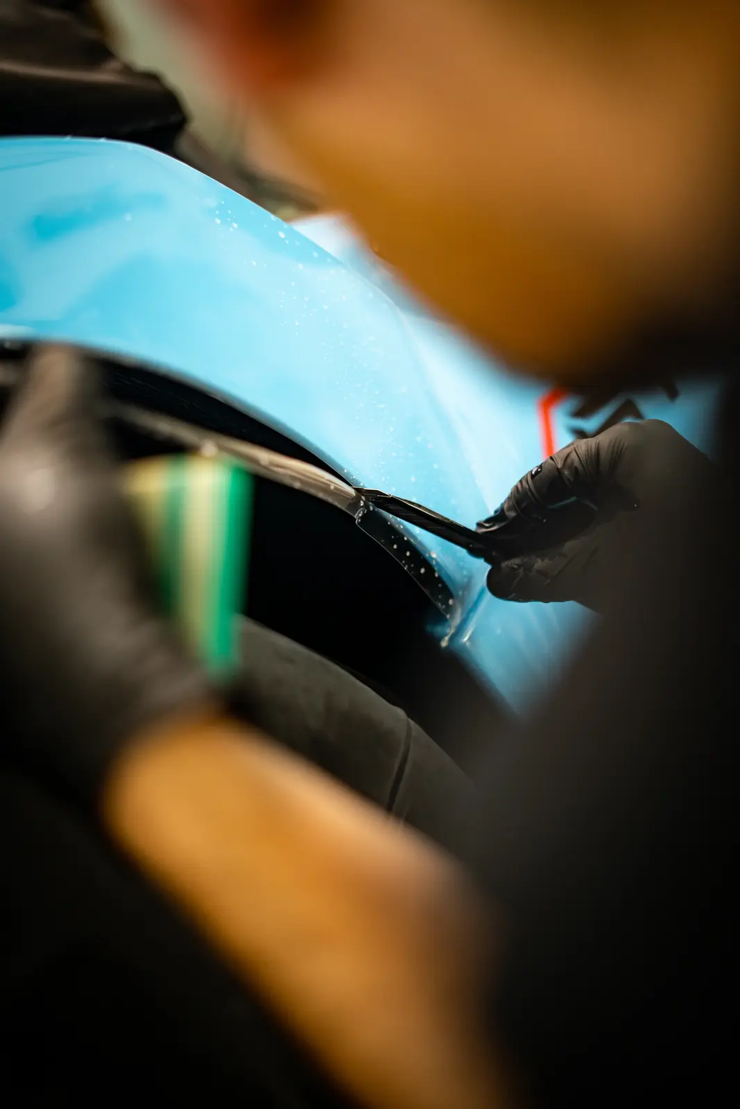 Close-up of gloved hands working film along the edge of a blue bonnet with a tool.