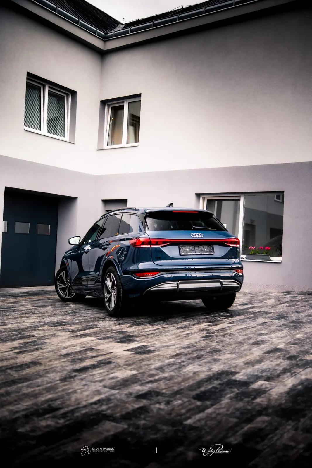 Zadní pohled na tmavě modré Audi Q6 e-tron před budovou provozovny.