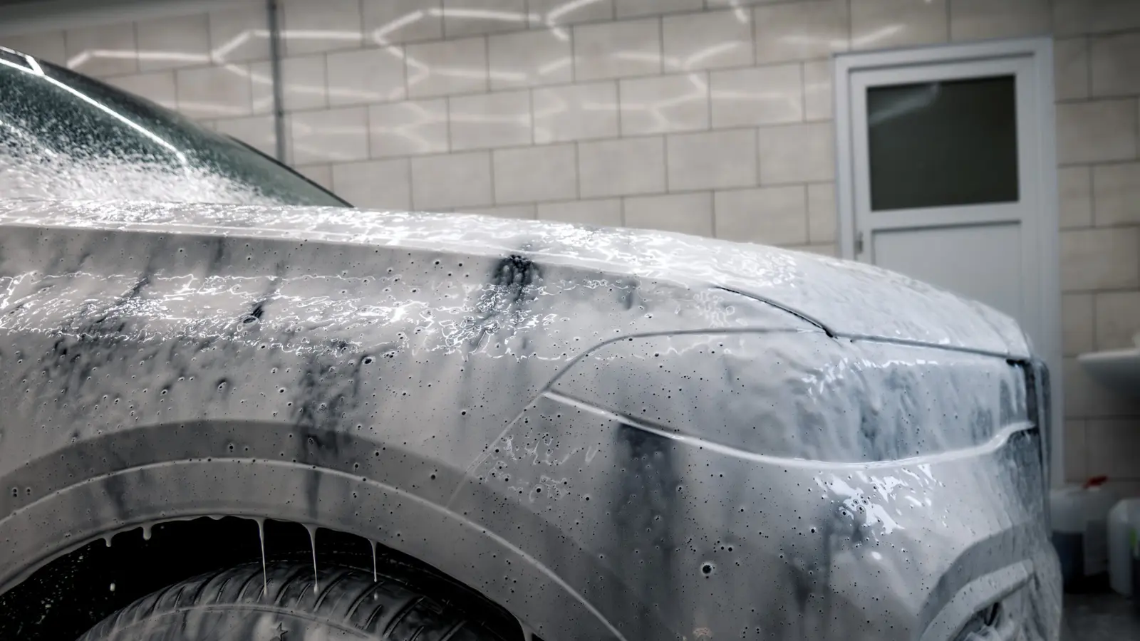A foam-covered car body during a hand wash, side view.