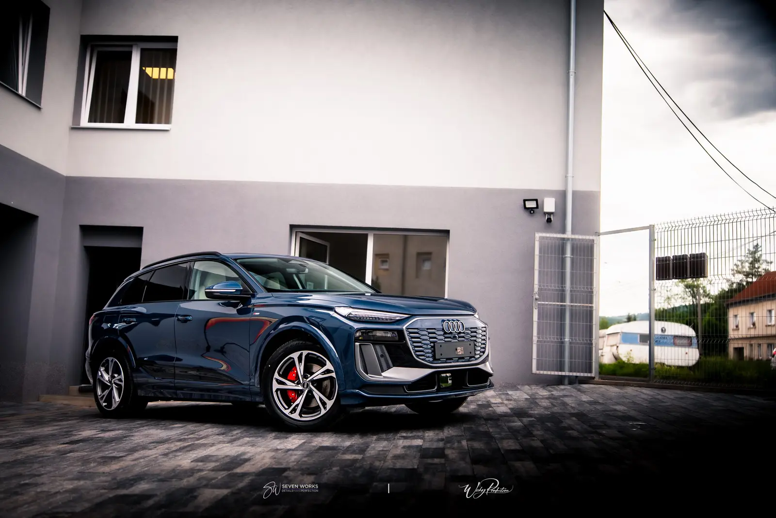 Tmavě modré Audi Q6 e-tron zepředu, zaparkované na dvorku provozovny Seven Works.
